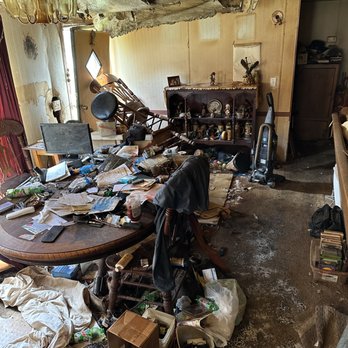 The hoarded property interior: collapsing ceiling, water-stained walls, dining table and floor buried in papers, clothing